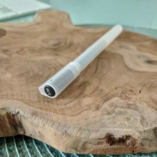 Noto Pepa Productfotografie MUJI Gel-Inktpen 0,38 mm in zwart op houten plank en computertoetsenbord op de achtergrond