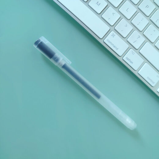Noto Pepa Productfotografie MUJI Gel-Inktpen 0,38 mm in zwart op bureau met computerkeyboard, zij-aanzicht van pen