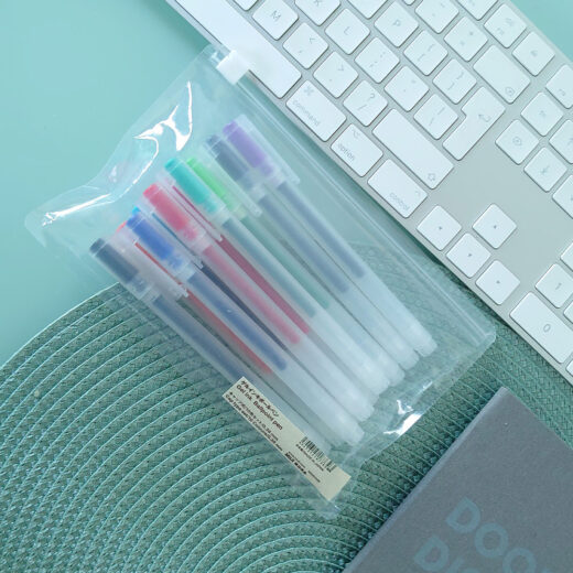 Noto Pepa Scene Productfotografie MUJI Gel Inktpen met Dop - Set van 10 (0,38mm) Kleuren in een herbruikbare opbergtas op bureau met toetsenbord en notitieblok, bovenaanzicht