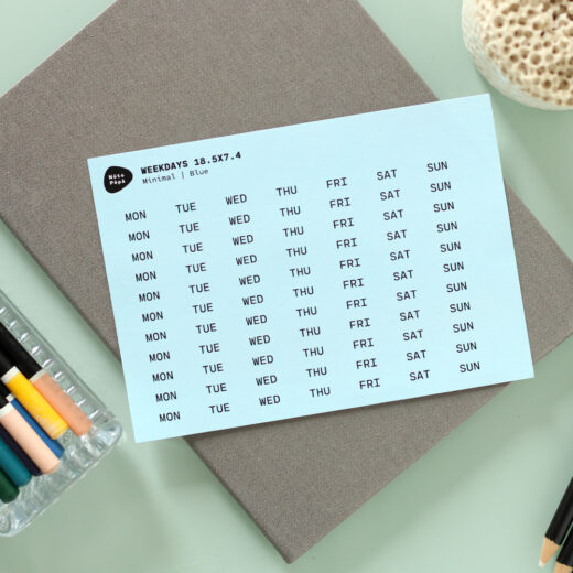 Noto Pepa Baby Blauw afgekorte Weekdagen Stickervel op werk bureau met notitieblok en kleurpotloden
